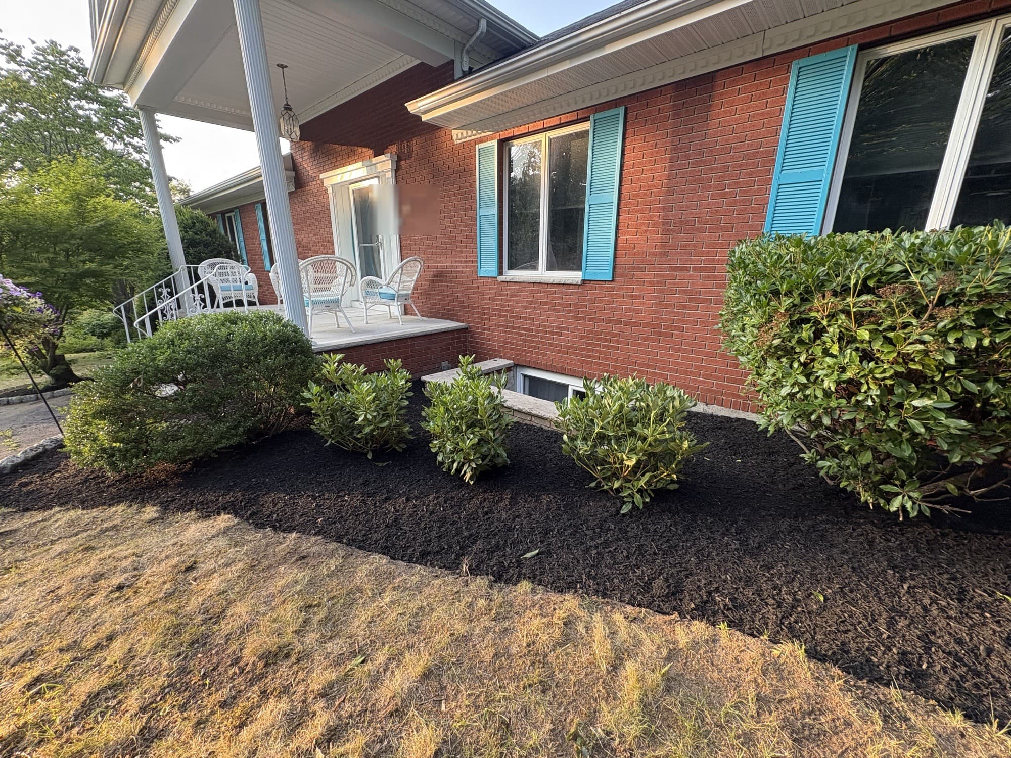 Brick house with teal shutters and freshly mulched foundation beds